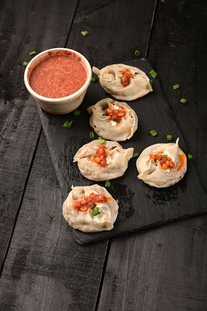 ours-journey A close-up of freshly steamed dumplings with spicy sauce served on a slate tray.