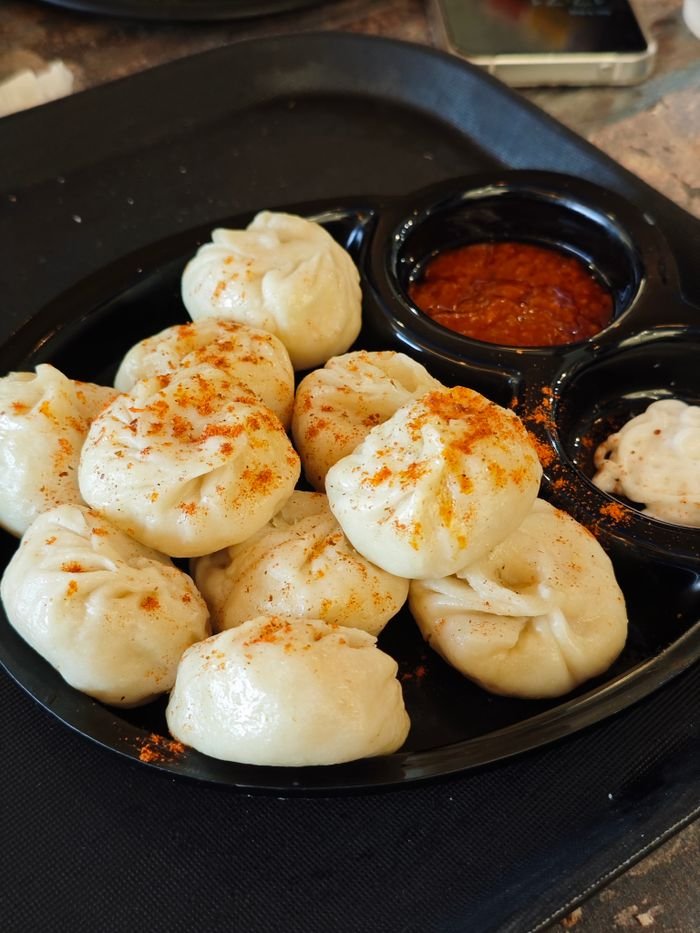 why-choose-us A plate of steamed momos served with spicy chutney on a black tray, perfect for a flavorful snack.