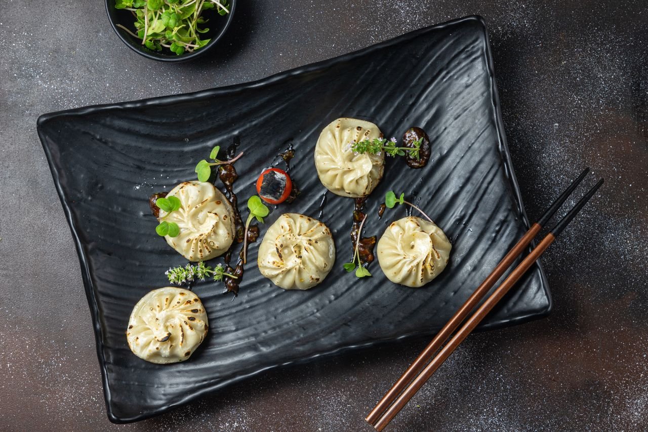 hero-img-02 Delicious steamed dumplings garnished with fresh microgreens on a black plate, perfect for food photography.